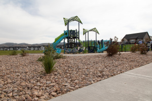 Playground at Mountain Ridge Park with slides, climbing structures, and overhead shade panels, shown from behind new rock landscaping.